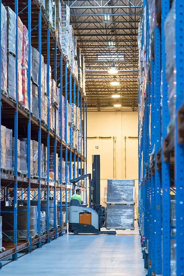 Reach truck operator carries a wrapped pallet down a racked aisle at a distribution center run by a 3PL provider